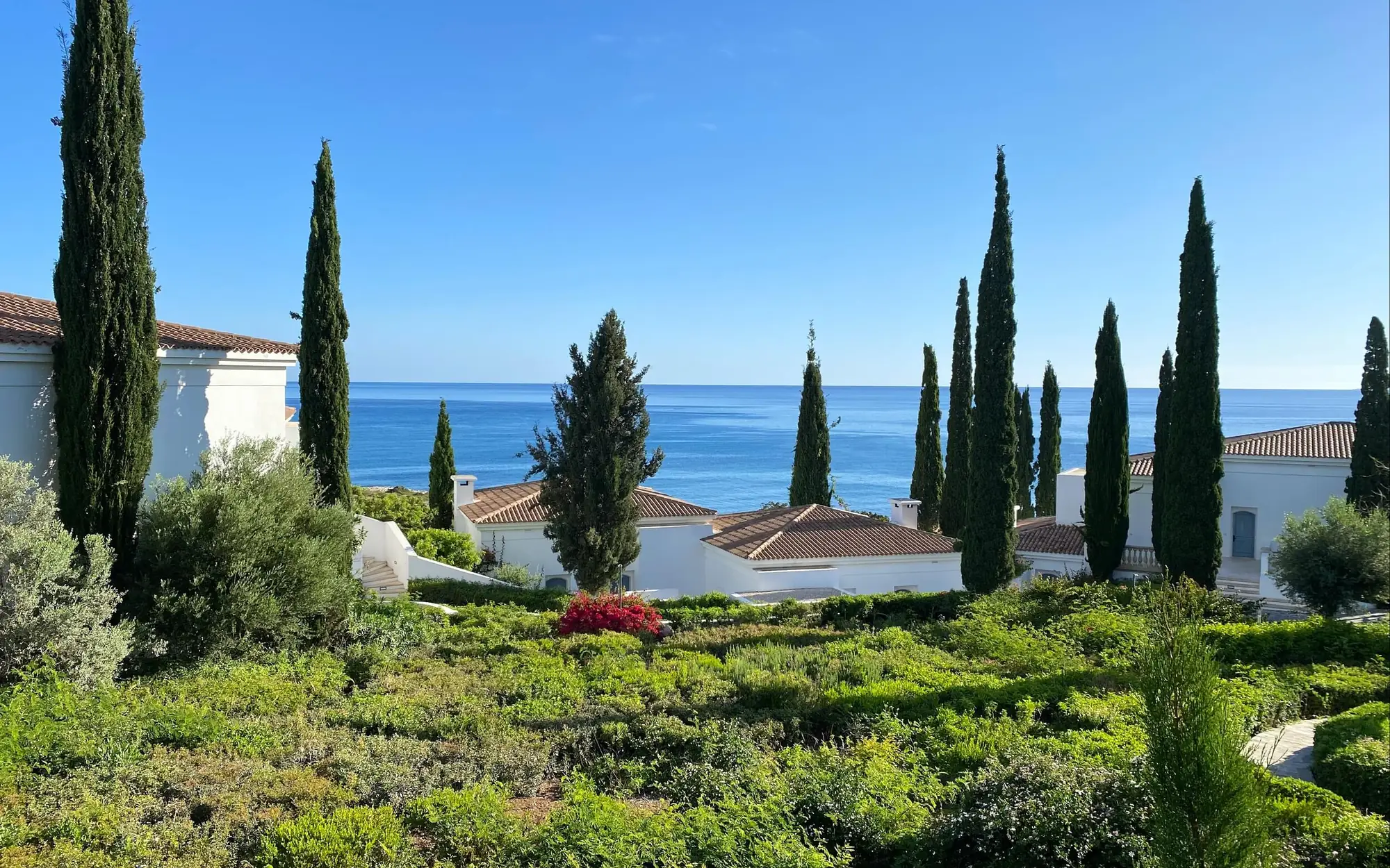 Villa garden with cypress trees overlooking white villas and the Mediterranean sea in Cyprus