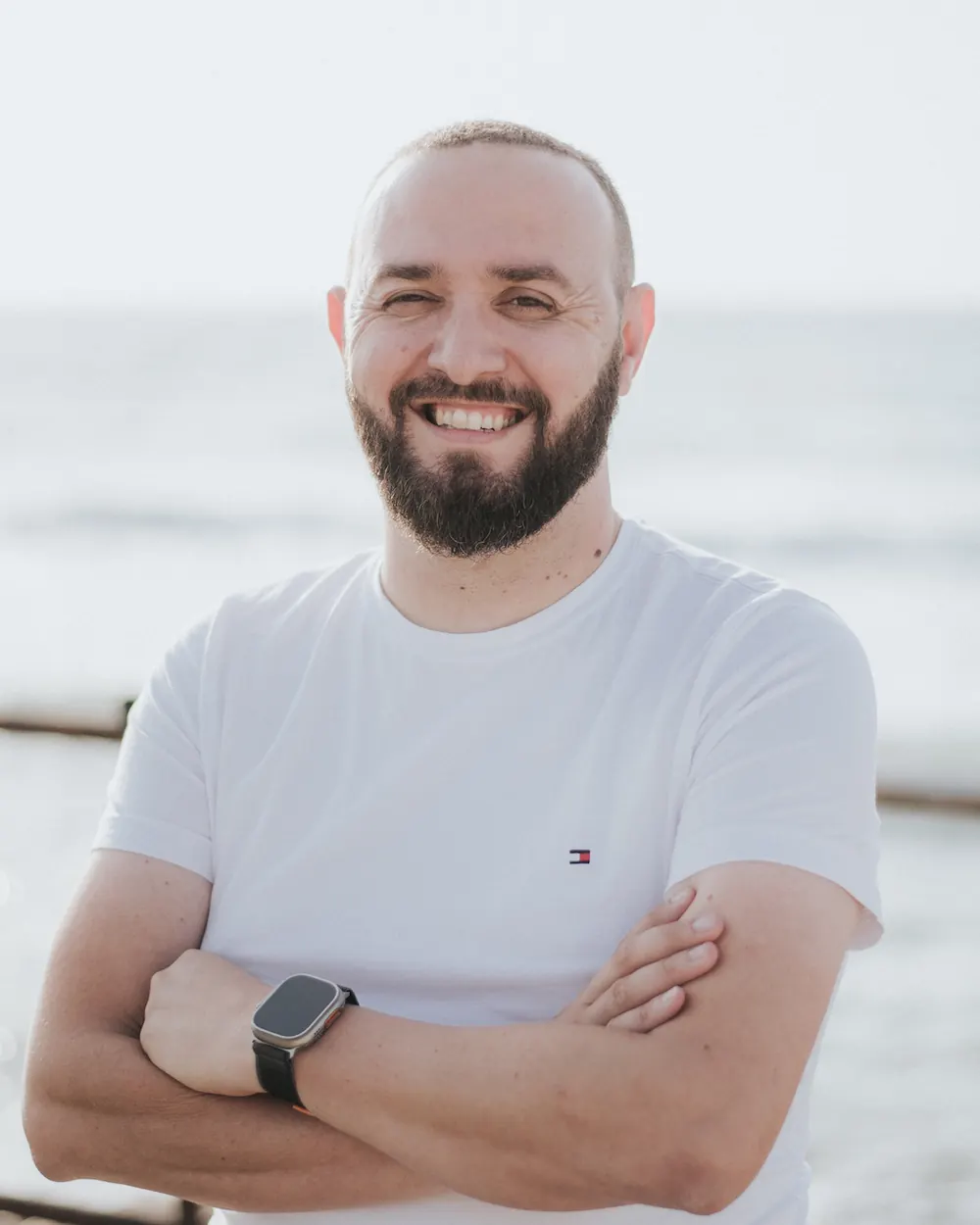 Nikolas Konstantinou, founder of RebaseCyprus, smiling with arms crossed by the sea in Paphos